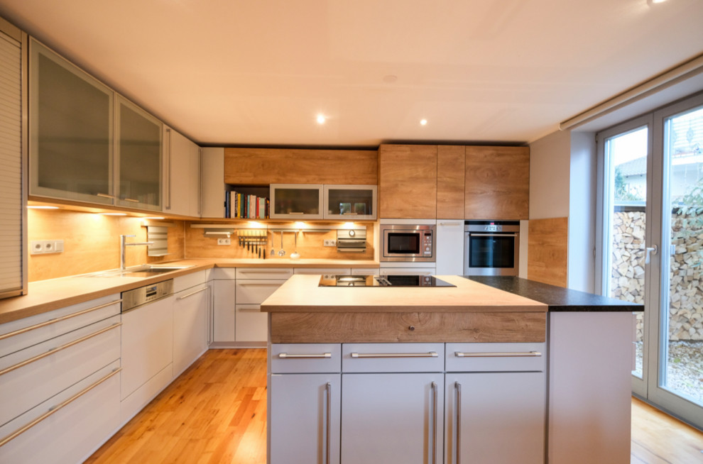 Große Wohnküche in L-Form mit Doppelwaschbecken, hellbraunen Holzschränken, Arbeitsplatte aus Holz, Küchenrückwand in Braun, Rückwand aus Holz, Küchengeräten aus Edelstahl, Kücheninsel und brauner Arbeitsplatte in München