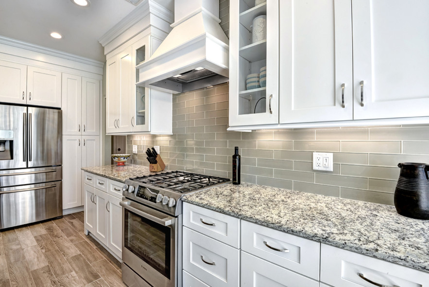 Photo of a large contemporary l-shaped eat-in kitchen in Charleston with an undermount sink, shaker cabinets, white cabinets, granite benchtops, grey splashback, glass tile splashback, stainless steel appliances, porcelain floors, with island and brown floor.