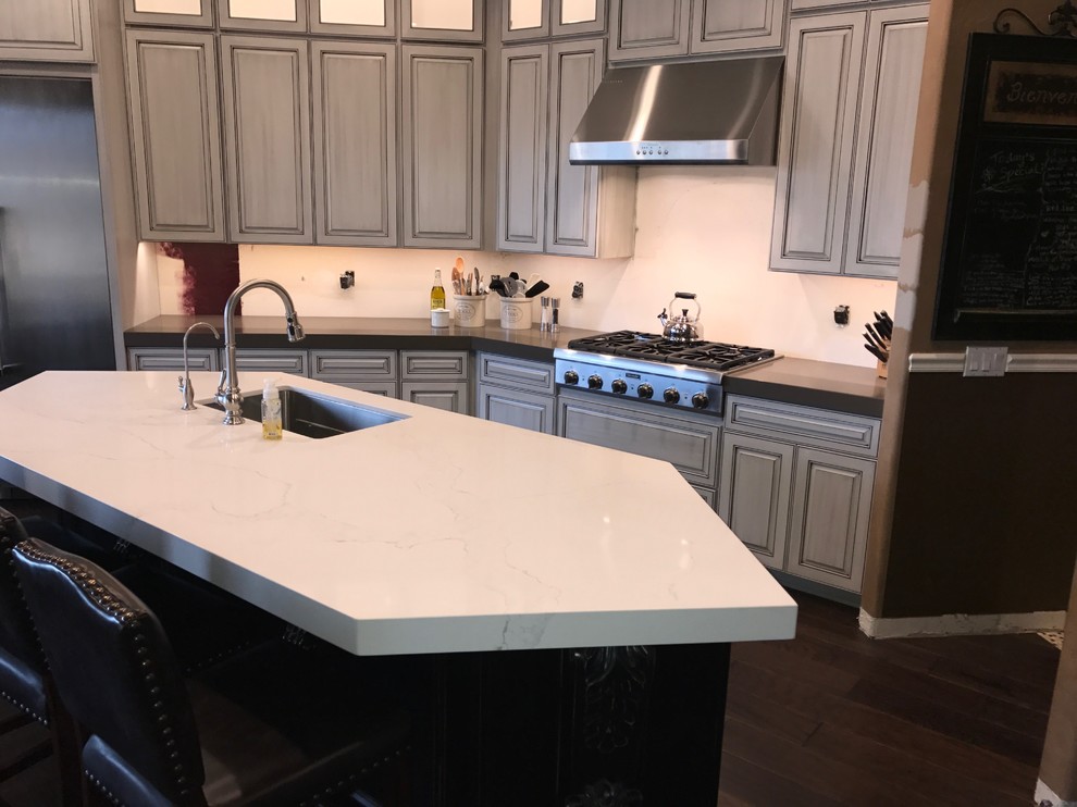 Example of a mid-sized transitional l-shaped dark wood floor and brown floor enclosed kitchen design in Phoenix with an undermount sink, raised-panel cabinets, white cabinets, quartz countertops, stainless steel appliances and an island