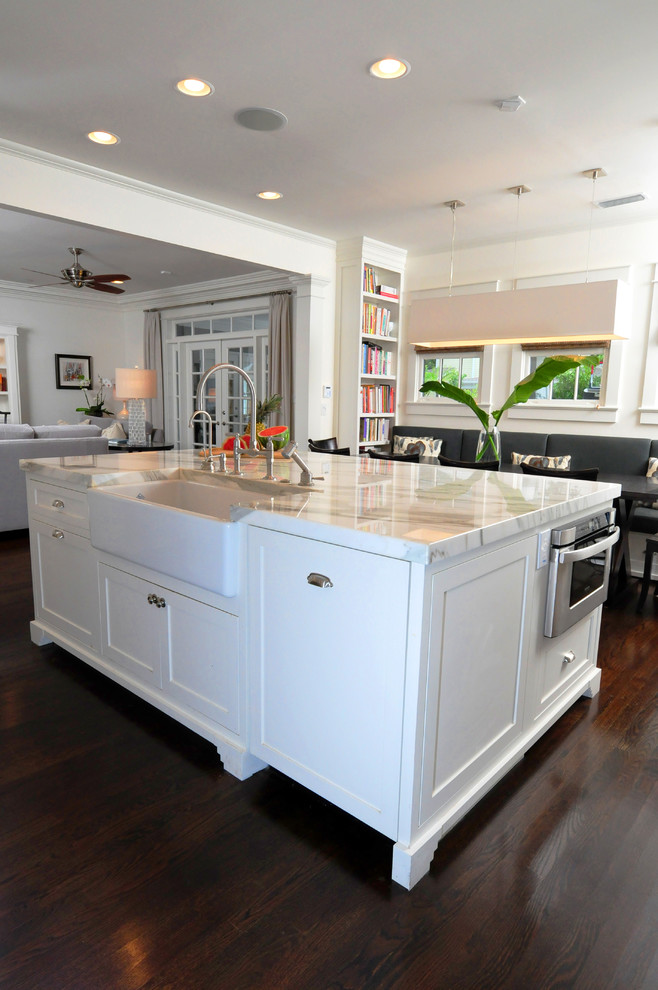 Large arts and crafts single-wall open plan kitchen in Tampa with a farmhouse sink, shaker cabinets, white cabinets, marble benchtops, dark hardwood floors, with island, brown floor, white splashback, subway tile splashback and stainless steel appliances.