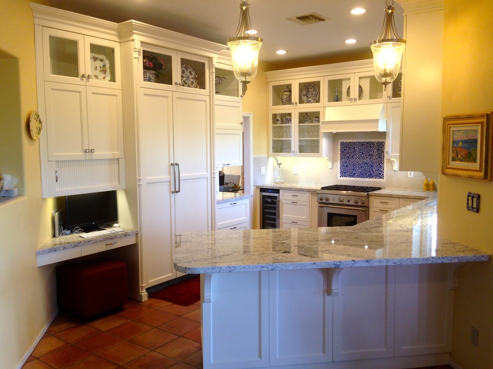 This is an example of a mid-sized traditional galley kitchen pantry in Orange County with beaded inset cabinets, white cabinets, granite benchtops, beige splashback, porcelain splashback, panelled appliances, terra-cotta floors, a peninsula, an undermount sink and brown floor.