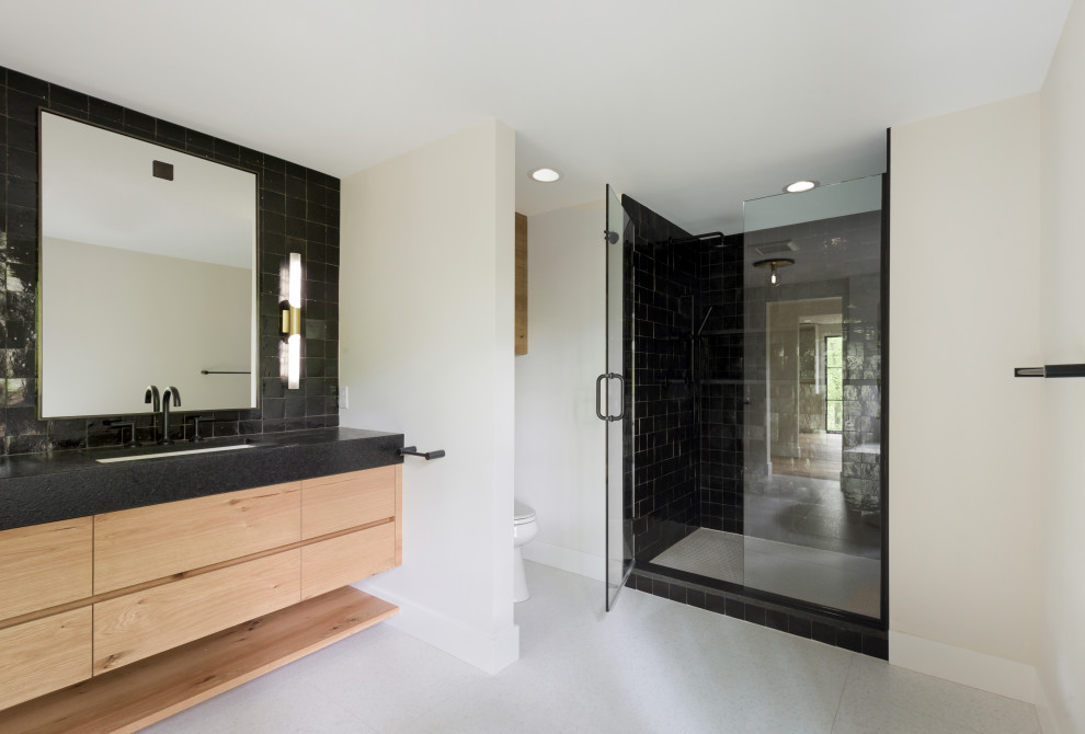 Inspiration for a large midcentury master bathroom in Minneapolis with medium wood cabinets, flat-panel cabinets, a freestanding tub, an alcove shower, a one-piece toilet, black tile, cement tile, white walls, terrazzo floors, an undermount sink, granite benchtops, white floor, a hinged shower door and black benchtops.