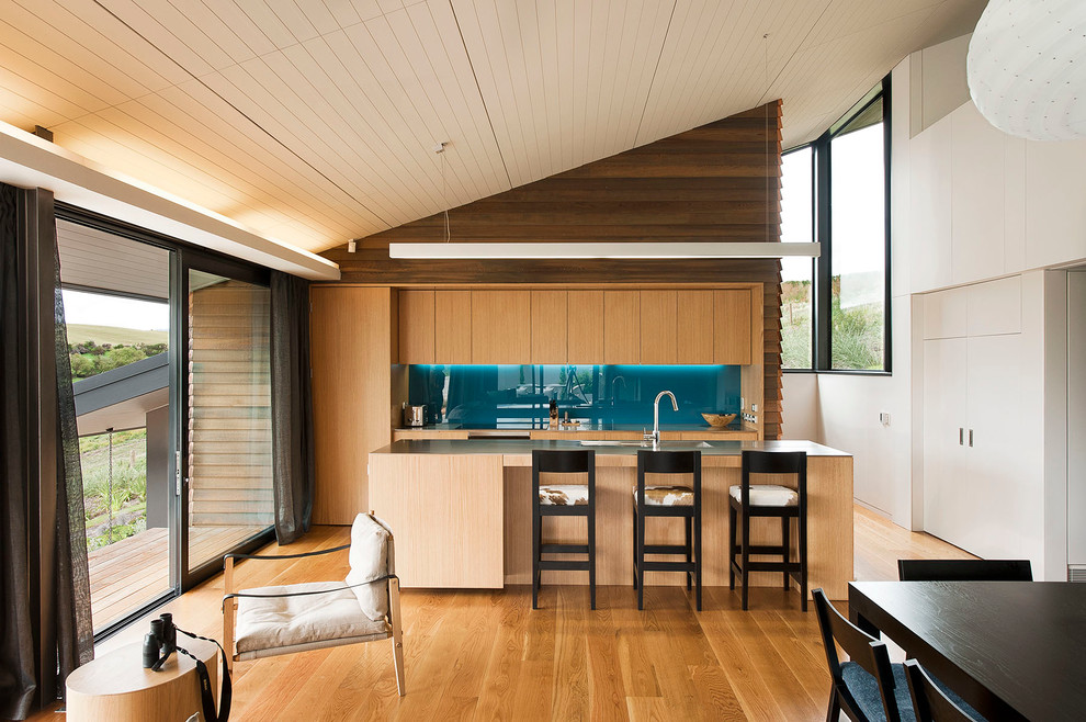 Inspiration for a contemporary galley open plan kitchen in Dunedin with an undermount sink, flat-panel cabinets, medium wood cabinets, blue splashback, glass sheet splashback, medium hardwood floors and with island.