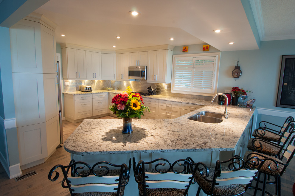 Large transitional u-shaped light wood floor kitchen photo in Toronto with a double-bowl sink, shaker cabinets, white cabinets, quartzite countertops, gray backsplash, subway tile backsplash, stainless steel appliances and a peninsula