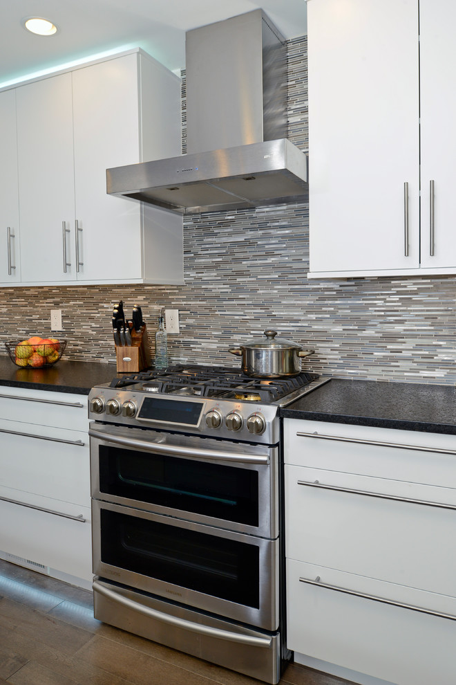 Inspiration for a mid-sized modern single-wall eat-in kitchen in DC Metro with a farmhouse sink, flat-panel cabinets, white cabinets, granite benchtops, brown splashback, mosaic tile splashback, stainless steel appliances, dark hardwood floors and with island.