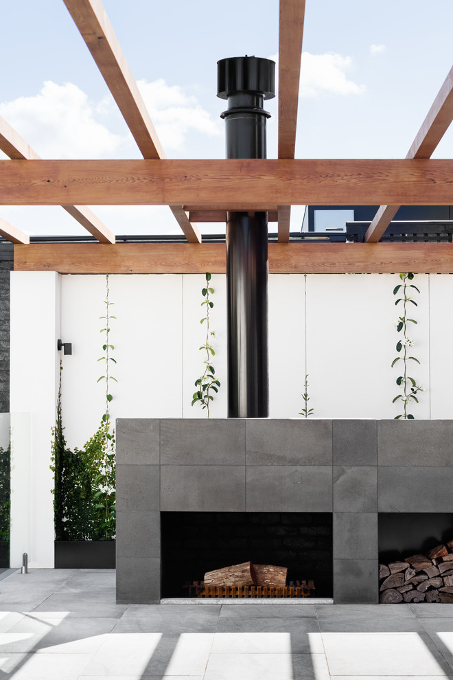 This is an example of an expansive modern backyard patio in Melbourne with a fire feature, natural stone pavers and a pergola.