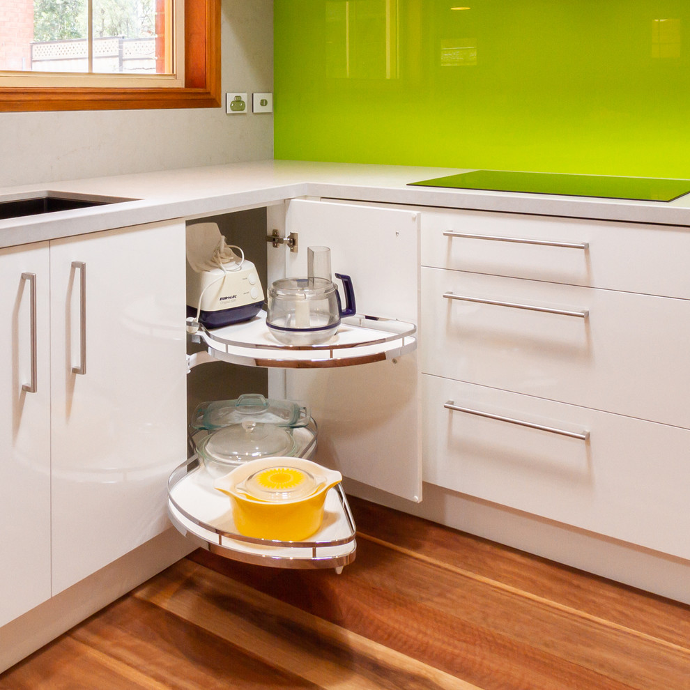 Inspiration for a mid-sized u-shaped eat-in kitchen in Melbourne with an undermount sink, flat-panel cabinets, white cabinets, quartz benchtops, green splashback, glass sheet splashback, black appliances, medium hardwood floors, a peninsula, brown floor and white benchtop.