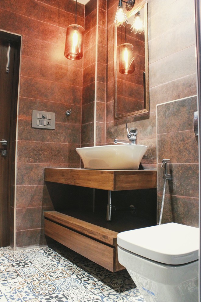 Design ideas for a mid-sized eclectic bathroom in Delhi with furniture-like cabinets, medium wood cabinets, an alcove shower, a wall-mount toilet, multi-coloured tile, cement tile, beige walls, cement tiles, a console sink, wood benchtops and a hinged shower door.