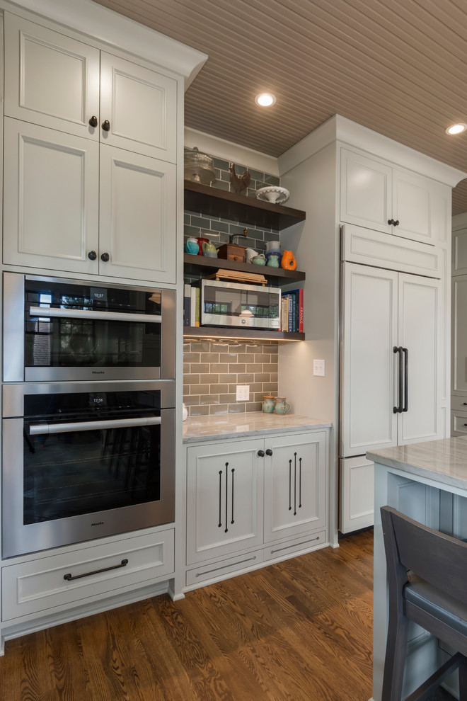 Mid-sized transitional u-shaped medium tone wood floor and brown floor enclosed kitchen photo in Seattle with an undermount sink, beaded inset cabinets, gray cabinets, quartzite countertops, gray backsplash, ceramic backsplash, paneled appliances and a peninsula