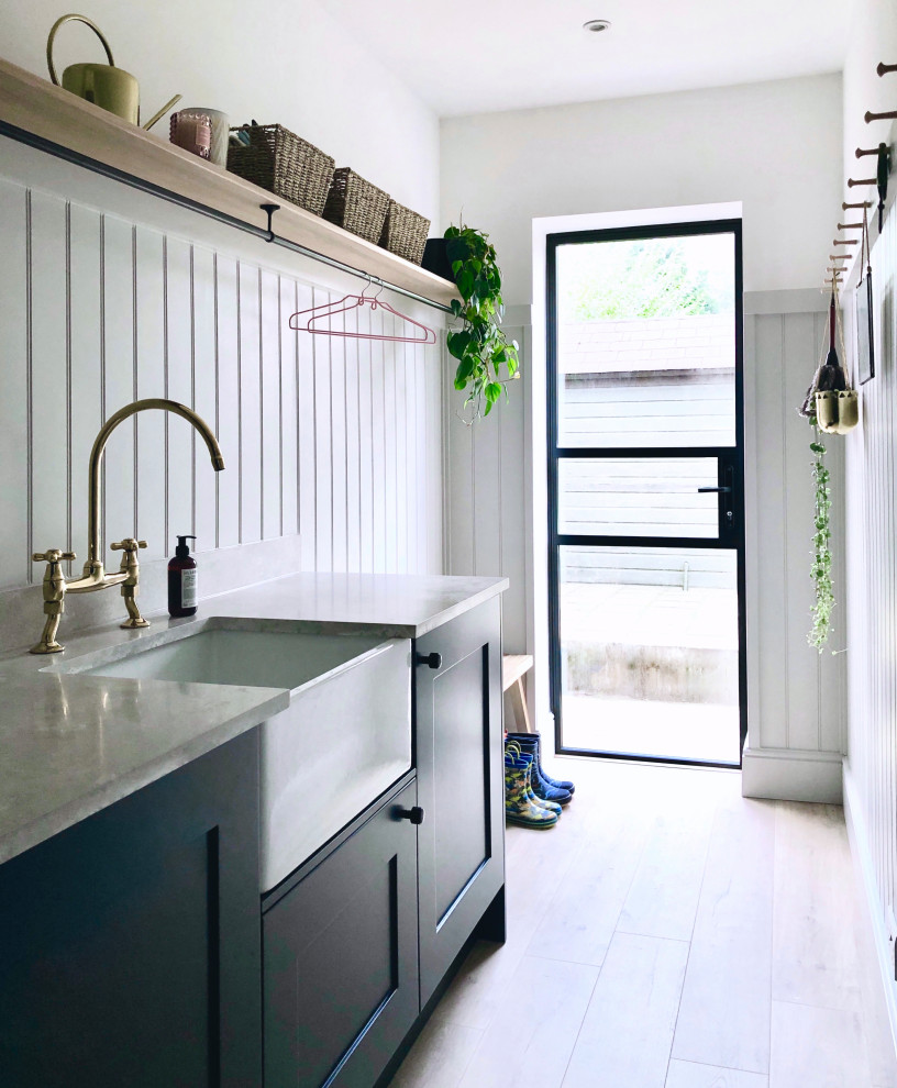 Inspiration for a small traditional single-wall utility room in Other with a farmhouse sink, shaker cabinets, blue cabinets, grey walls, laminate floors, an integrated washer and dryer, beige floor, grey benchtop and planked wall panelling.