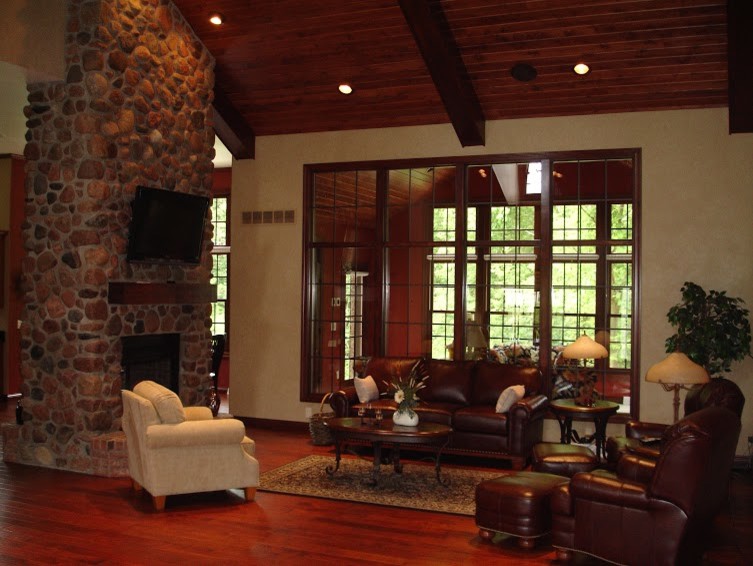 Large mountain style open concept dark wood floor family room photo with beige walls, a two-sided fireplace, a stone fireplace and a wall-mounted tv