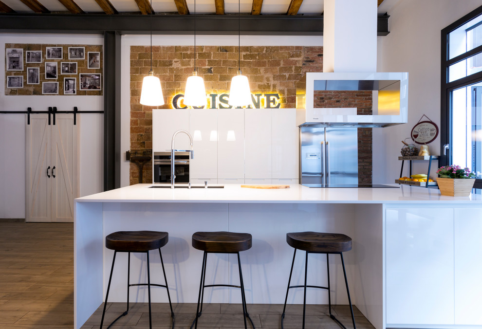 This is an example of a large contemporary single-wall open plan kitchen in Barcelona with a submerged sink, flat-panel cabinets, white cabinets, laminate countertops, stainless steel appliances, porcelain flooring, an island, brown floors, white worktops and exposed beams.