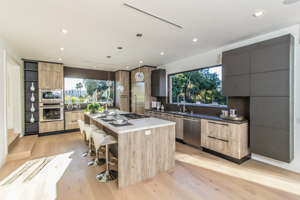Photo of a large contemporary l-shaped eat-in kitchen in Los Angeles with a drop-in sink, flat-panel cabinets, beige cabinets, quartzite benchtops, grey splashback, window splashback, stainless steel appliances, light hardwood floors, with island, beige floor and white benchtop.