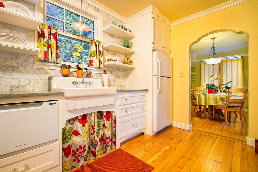 Example of a mid-sized classic light wood floor and brown floor enclosed kitchen design in Sacramento with a farmhouse sink, shaker cabinets, white cabinets, white appliances, quartzite countertops, white backsplash and marble backsplash