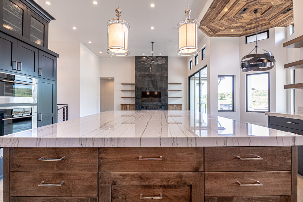 Large country u-shaped open plan kitchen in Salt Lake City with an undermount sink, glass-front cabinets, black cabinets, quartzite benchtops, beige splashback, stone slab splashback, stainless steel appliances, concrete floors, with island, grey floor and beige benchtop.
