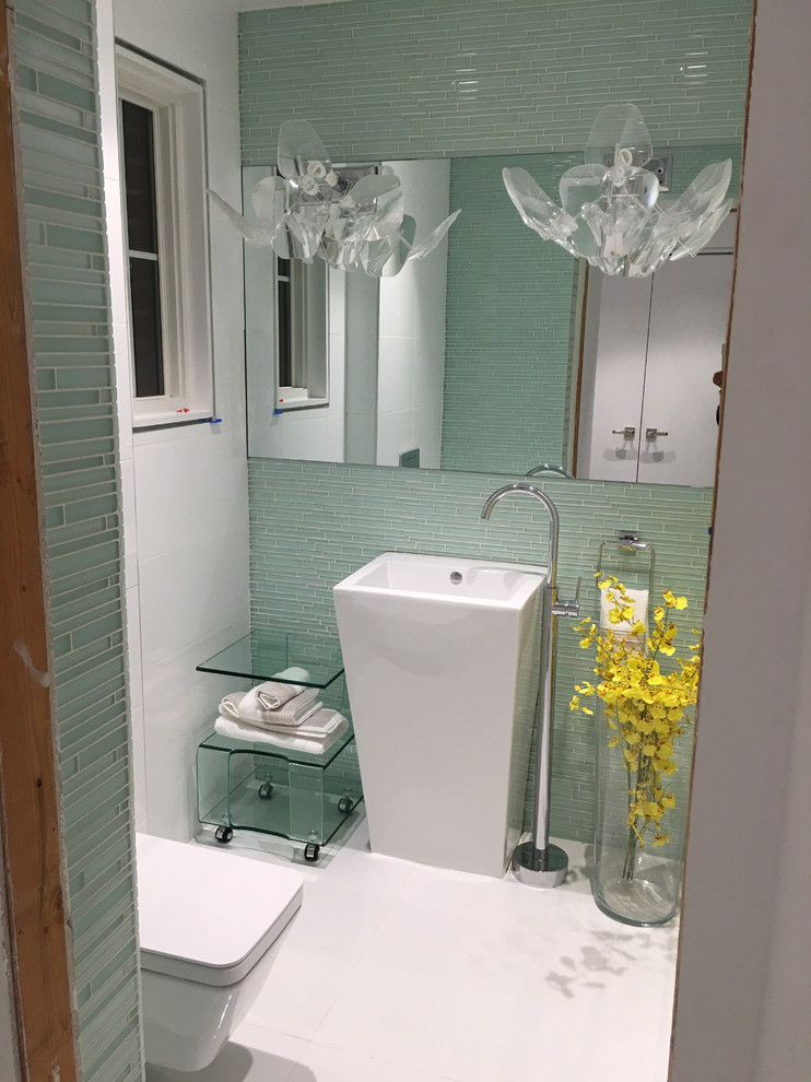 Mid-sized modern powder room in New York with glass-front cabinets, a one-piece toilet, glass tile, white walls, marble floors and a pedestal sink.