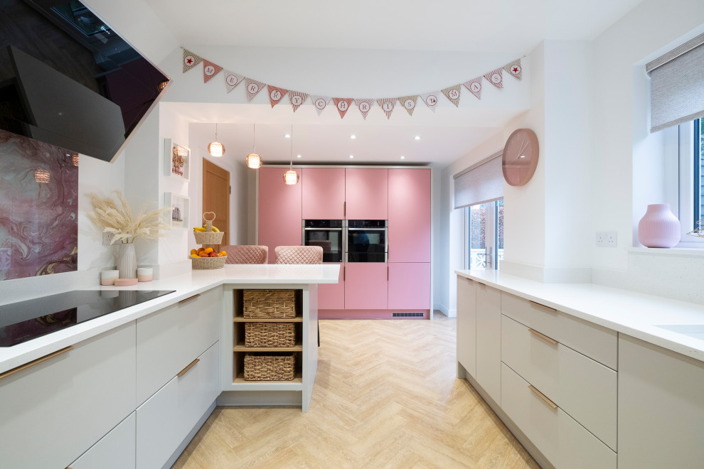 Design ideas for a mid-sized contemporary u-shaped eat-in kitchen in Cardiff with an integrated sink, flat-panel cabinets, pink cabinets, quartzite benchtops, pink splashback, glass sheet splashback, stainless steel appliances, laminate floors, a peninsula and white benchtop.