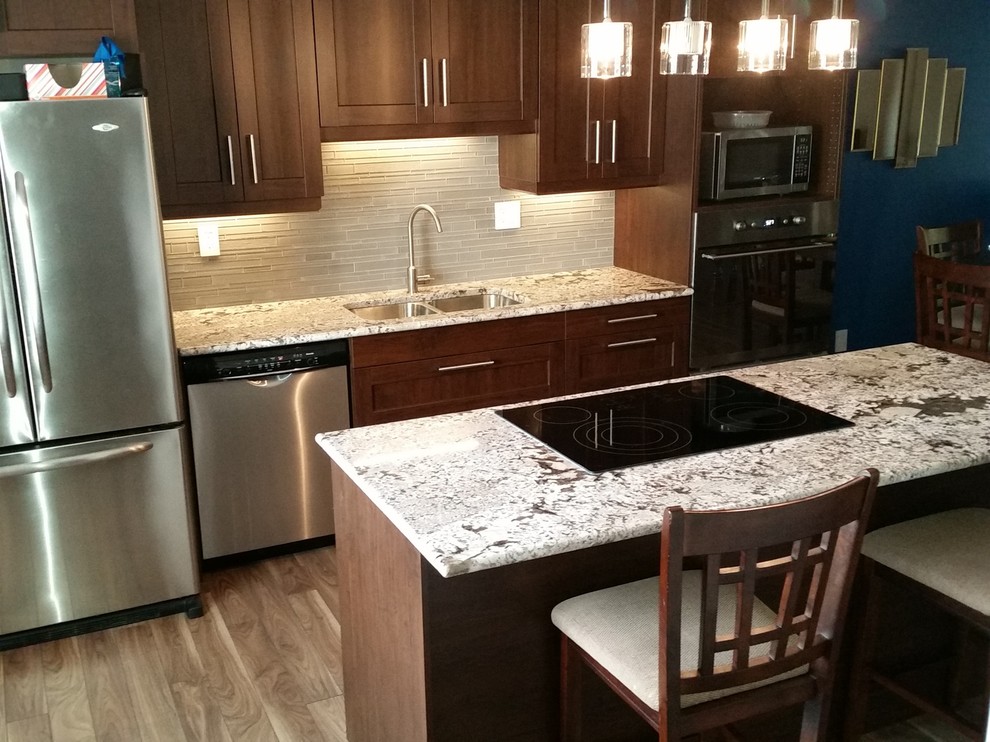 Large transitional medium tone wood floor and brown floor kitchen photo with a double-bowl sink, shaker cabinets, dark wood cabinets, granite countertops, gray backsplash, matchstick tile backsplash, stainless steel appliances and an island