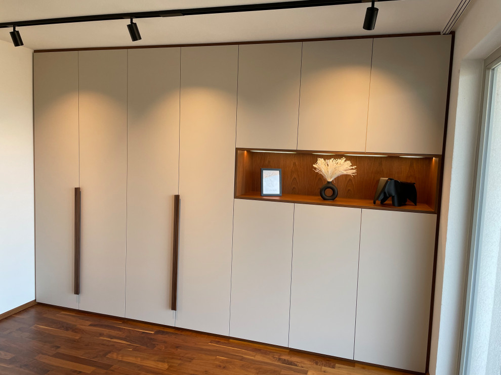 Imagen de armario y vestidor contemporáneo de tamaño medio con a medida, armarios con paneles lisos, puertas de armario grises, suelo de madera oscura, suelo marrón y papel pintado