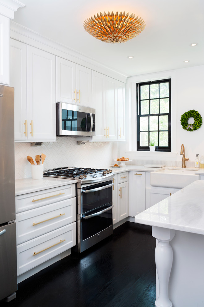 This is an example of a transitional galley kitchen in DC Metro with white cabinets, quartzite benchtops, white splashback, subway tile splashback, stainless steel appliances, painted wood floors, shaker cabinets, a farmhouse sink and black floor.