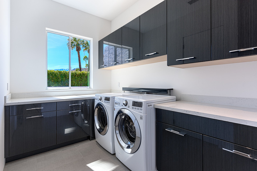 Design ideas for a large modern l-shaped dedicated laundry room in Los Angeles with flat-panel cabinets, quartz benchtops, white walls, porcelain floors, a side-by-side washer and dryer and black cabinets.