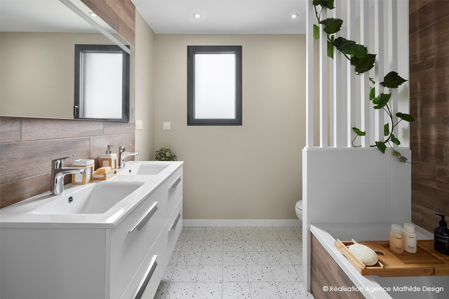 This is an example of a mid-sized contemporary bathroom in Nantes with an undermount tub, a wall-mount toilet, brown tile, wood-look tile, terrazzo floors, multi-coloured floor, white benchtops, an enclosed toilet and a double vanity.