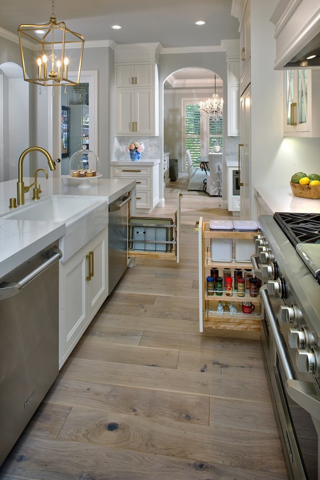 Mid-sized transitional u-shaped light wood floor eat-in kitchen photo in Sacramento with a farmhouse sink, white cabinets, gray backsplash, stainless steel appliances, an island and white countertops