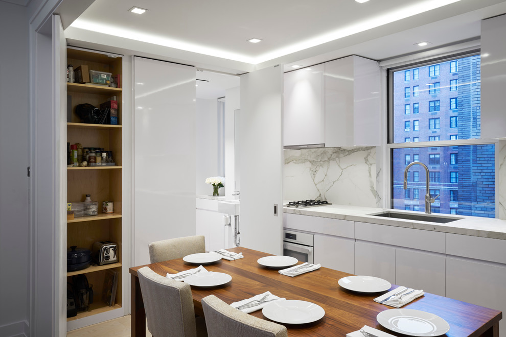 Inspiration for a mid-sized contemporary galley eat-in kitchen in New York with flat-panel cabinets, white cabinets, marble benchtops, white splashback, stainless steel appliances, light hardwood floors and no island.