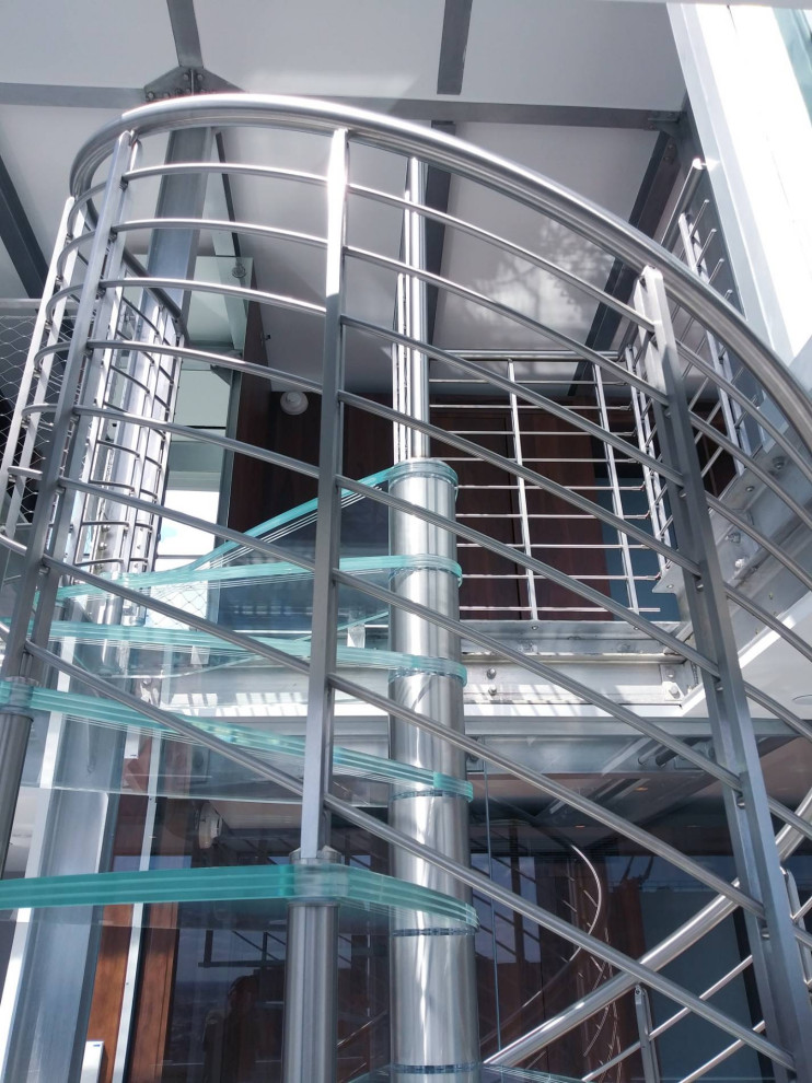 Cette photo montre un grand escalier hélicoïdal industriel avec des marches en verre et un garde-corps en métal.