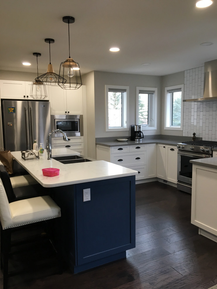 Inspiration for a mid-sized transitional u-shaped dark wood floor and brown floor kitchen remodel with a farmhouse sink, shaker cabinets, white cabinets, quartzite countertops, white backsplash, subway tile backsplash, stainless steel appliances, an island and gray countertops