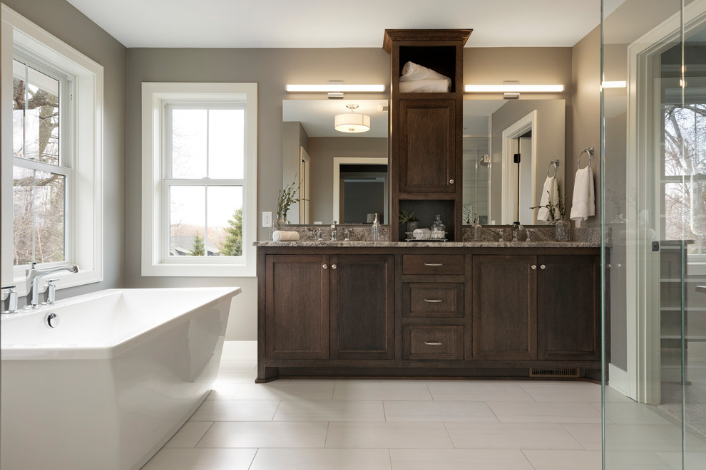 Design ideas for a large transitional master bathroom in Minneapolis with shaker cabinets, dark wood cabinets, a freestanding tub, a corner shower, a two-piece toilet, grey walls, ceramic floors, an undermount sink, granite benchtops, grey floor and grey benchtops.