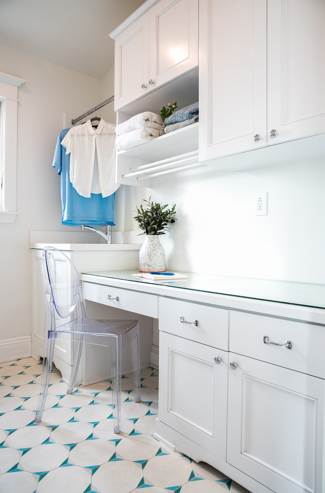 Inspiration for a small beach style galley dedicated laundry room in Los Angeles with an undermount sink, shaker cabinets, white cabinets, glass benchtops, ceramic floors, a side-by-side washer and dryer, blue floor, white benchtop and white walls.