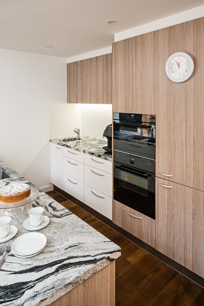Inspiration for a large contemporary galley eat-in kitchen in Melbourne with an undermount sink, flat-panel cabinets, medium wood cabinets, granite benchtops, white splashback, glass sheet splashback, black appliances, medium hardwood floors, multiple islands, brown floor and multi-coloured benchtop.