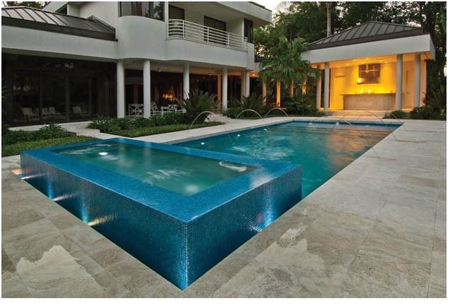This is an example of a large modern backyard rectangular lap pool in Tampa with a hot tub and natural stone pavers.