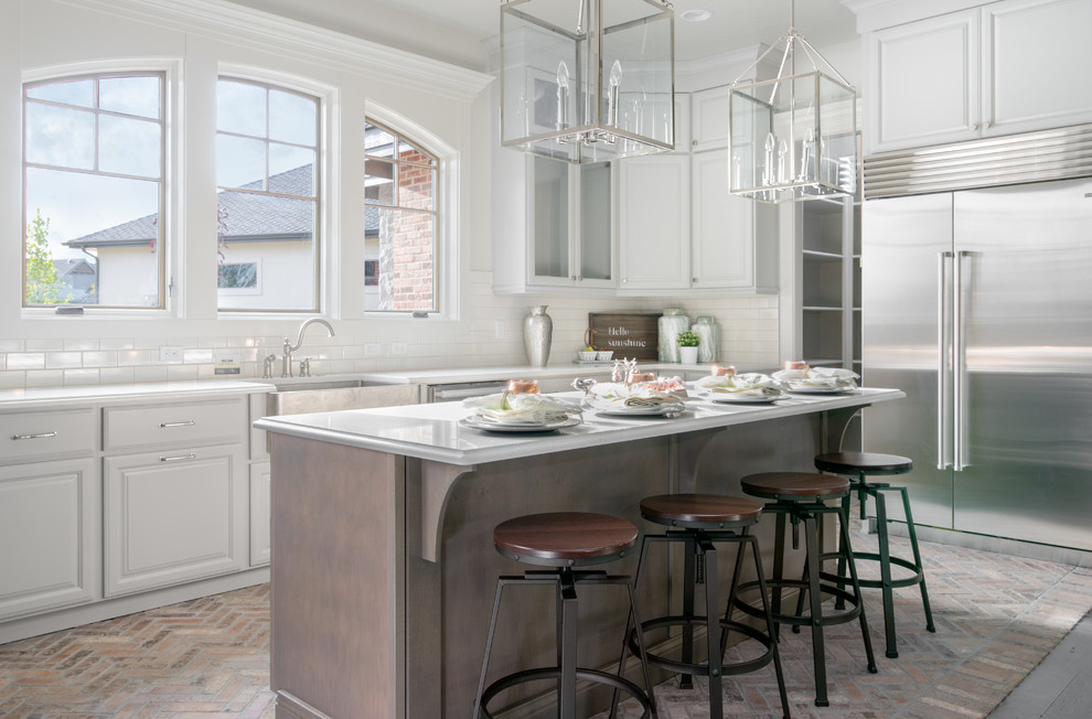 Design ideas for a traditional l-shaped kitchen in Boise with a farmhouse sink, raised-panel cabinets, white cabinets, white splashback, subway tile splashback, stainless steel appliances, brick floors and with island.