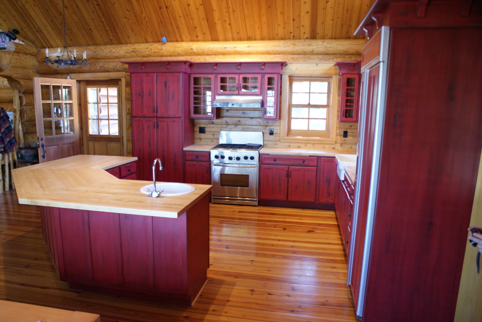 This is an example of a large country l-shaped eat-in kitchen in Other with a farmhouse sink, recessed-panel cabinets, red cabinets, wood benchtops, brown splashback, timber splashback, panelled appliances, medium hardwood floors, with island and brown floor.