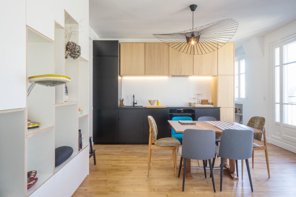 Photo of a small midcentury single-wall eat-in kitchen in Paris with an undermount sink, white splashback, panelled appliances, flat-panel cabinets, black cabinets, medium hardwood floors, no island and brown floor.