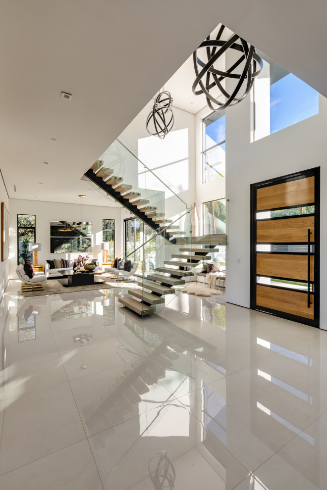Expansive contemporary front door in Los Angeles with white walls, porcelain floors, a pivot front door, a light wood front door and white floor.