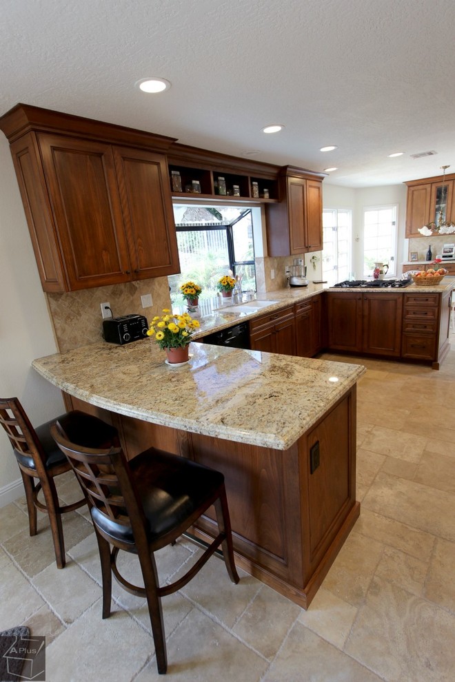 Photo of a mid-sized transitional u-shaped eat-in kitchen in Orange County with a double-bowl sink, recessed-panel cabinets, medium wood cabinets, granite benchtops, brown splashback, stone tile splashback, black appliances, porcelain floors and a peninsula.