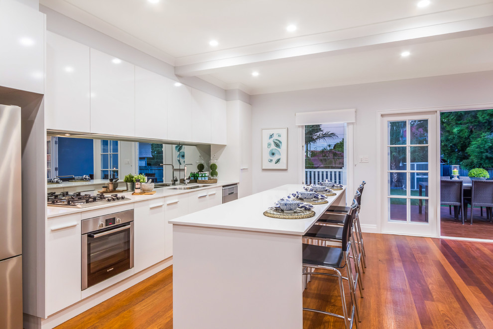 Inspiration for a contemporary kitchen in Brisbane with flat-panel cabinets, white cabinets, quartz benchtops, metallic splashback, mirror splashback, stainless steel appliances and with island.