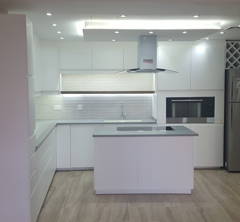 Example of a large minimalist l-shaped ceramic tile kitchen pantry design with an integrated sink, flat-panel cabinets, white cabinets, ceramic backsplash, black appliances and an island