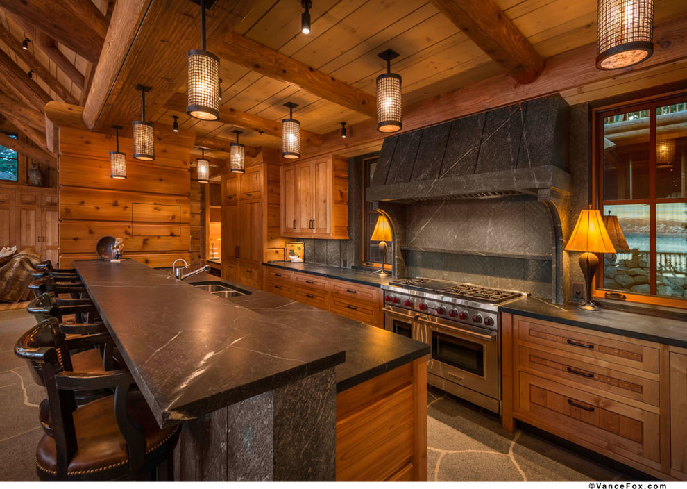 This is an example of a country galley open plan kitchen in Sacramento with a double-bowl sink, raised-panel cabinets, medium wood cabinets, soapstone benchtops, black splashback, stone slab splashback and stainless steel appliances.