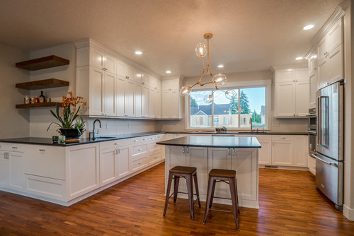 Example of an u-shaped brown floor open concept kitchen design in Portland with white cabinets, beige backsplash, stainless steel appliances, an island, black countertops and shaker cabinets