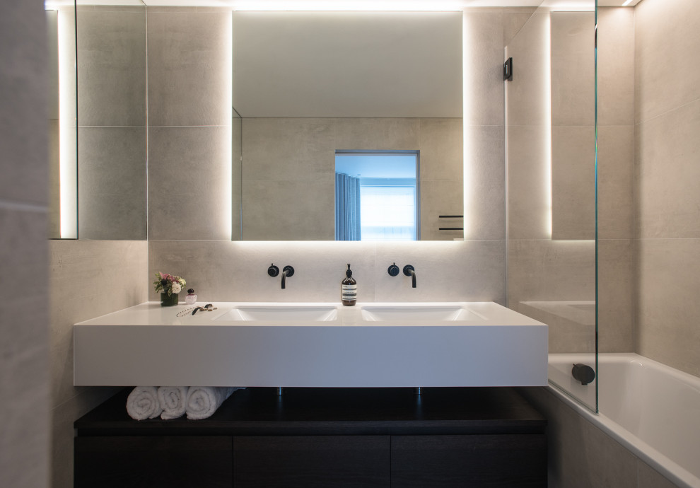Mid-sized contemporary master bathroom in London with flat-panel cabinets, dark wood cabinets, a drop-in tub, a shower/bathtub combo, a wall-mount toilet, gray tile, porcelain tile, grey walls, porcelain floors, an integrated sink, wood benchtops, grey floor, a hinged shower door, white benchtops, a double vanity, a floating vanity and recessed.