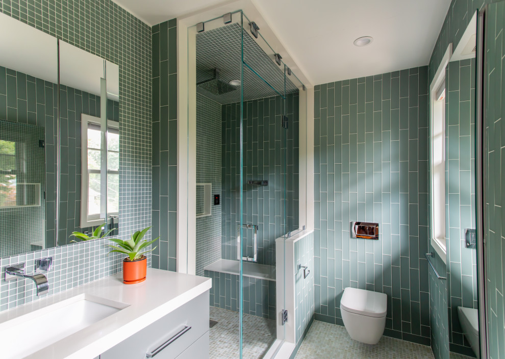 Пример оригинального дизайна: главная ванная комната среднего размера в стиле модернизм с плоскими фасадами, серыми фасадами, угловым душем, инсталляцией, зеленой плиткой, стеклянной плиткой, зелеными стенами, полом из мозаичной плитки, врезной раковиной, столешницей из искусственного кварца, разноцветным полом, душем с распашными дверями, белой столешницей, сиденьем для душа, тумбой под одну раковину и напольной тумбой