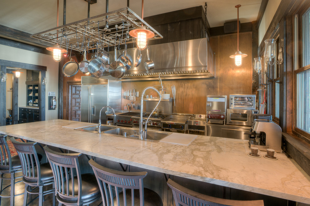 Industrial galley kitchen in Seattle with a triple-bowl sink, metallic splashback and stainless steel appliances.