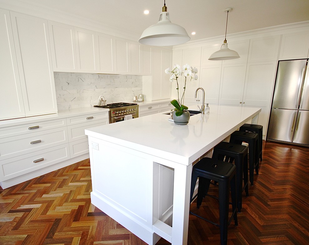 Photo of a large transitional l-shaped open plan kitchen in Sydney with an undermount sink, shaker cabinets, white cabinets, quartz benchtops, white splashback, stone tile splashback, stainless steel appliances, dark hardwood floors and with island.