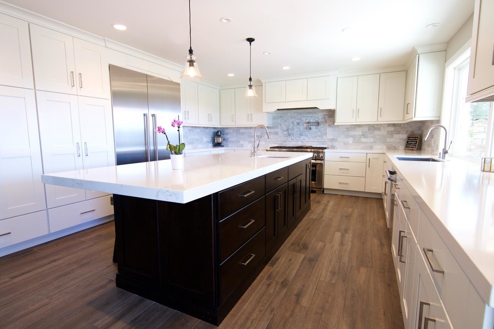 This is an example of a large contemporary u-shaped open plan kitchen in Orange County with an undermount sink, shaker cabinets, white cabinets, marble benchtops, grey splashback, marble splashback, stainless steel appliances, medium hardwood floors, with island and brown floor.