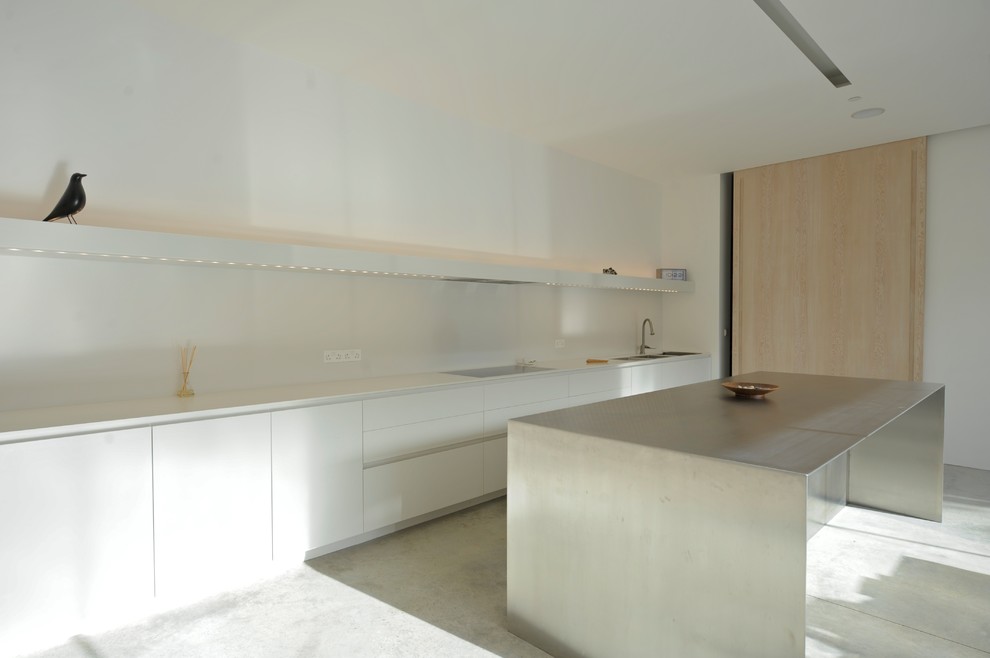 This is an example of an expansive contemporary galley open plan kitchen in London with an integrated sink, flat-panel cabinets, white cabinets, solid surface benchtops, white splashback, stainless steel appliances, concrete floors and with island.