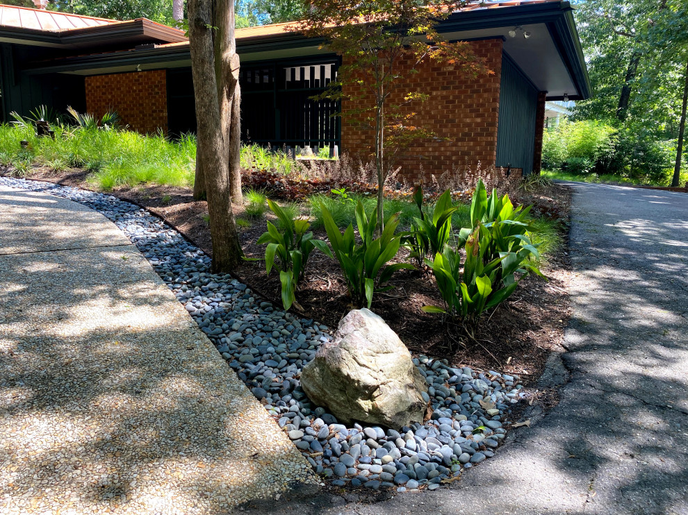 This is an example of a large midcentury front yard partial sun xeriscape in Raleigh with with waterfall and river rock.